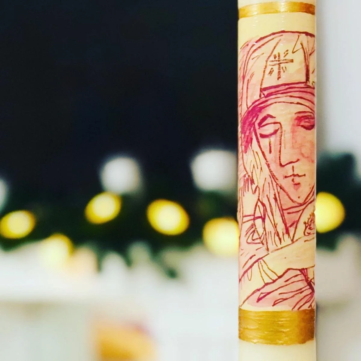 Detalle de un rostro pintado a mano en trazo fino sobre una vela de bautizo