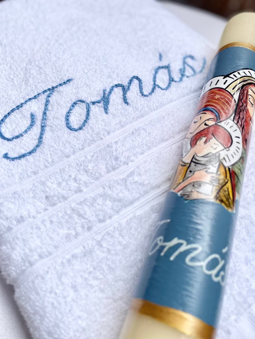 Toalla de bautizo bordada con el nombre Tomás, junto a la vela a juego